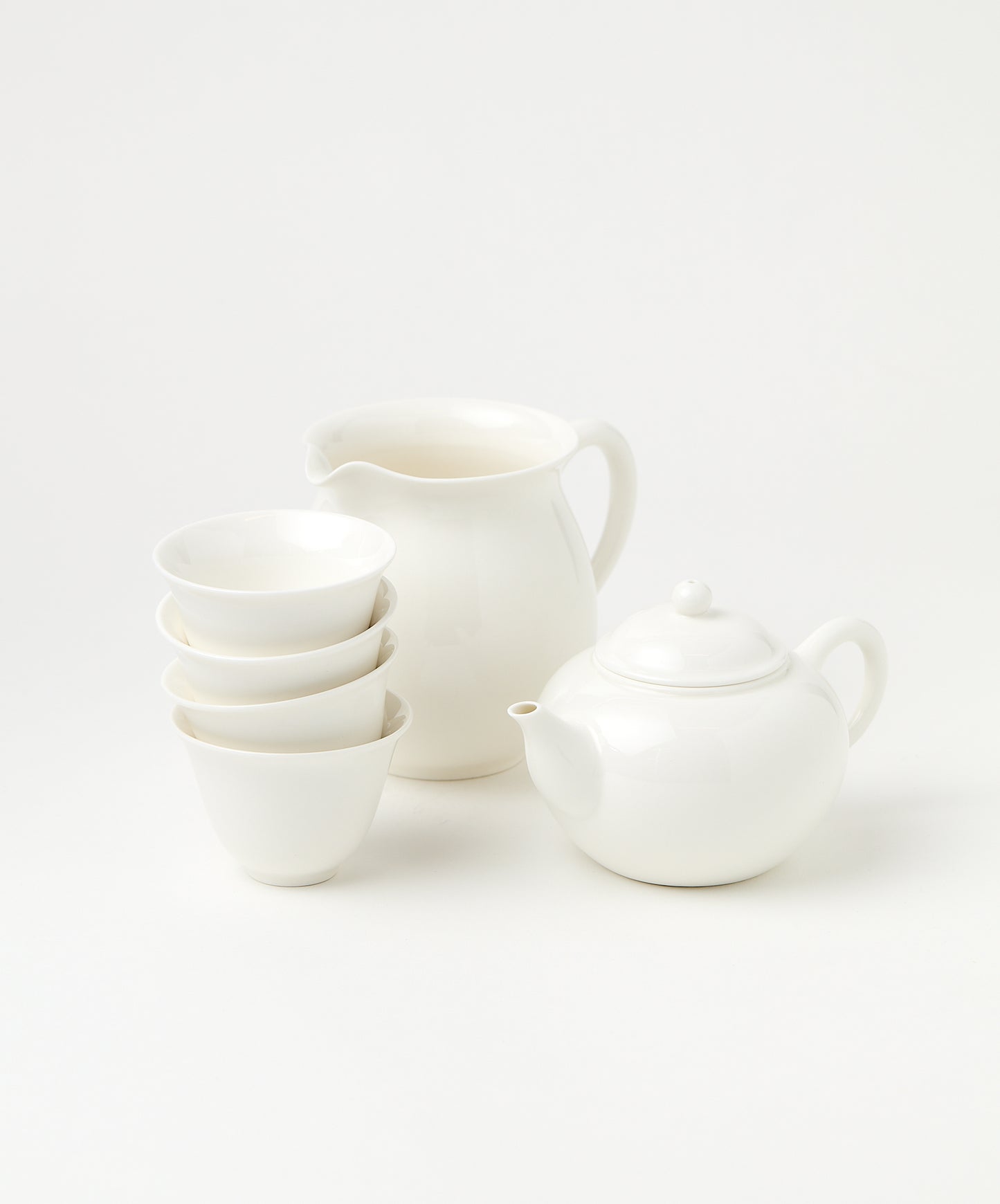 A porcelain brewing set featuring a white teapot, pitcher, and four stacked cups.