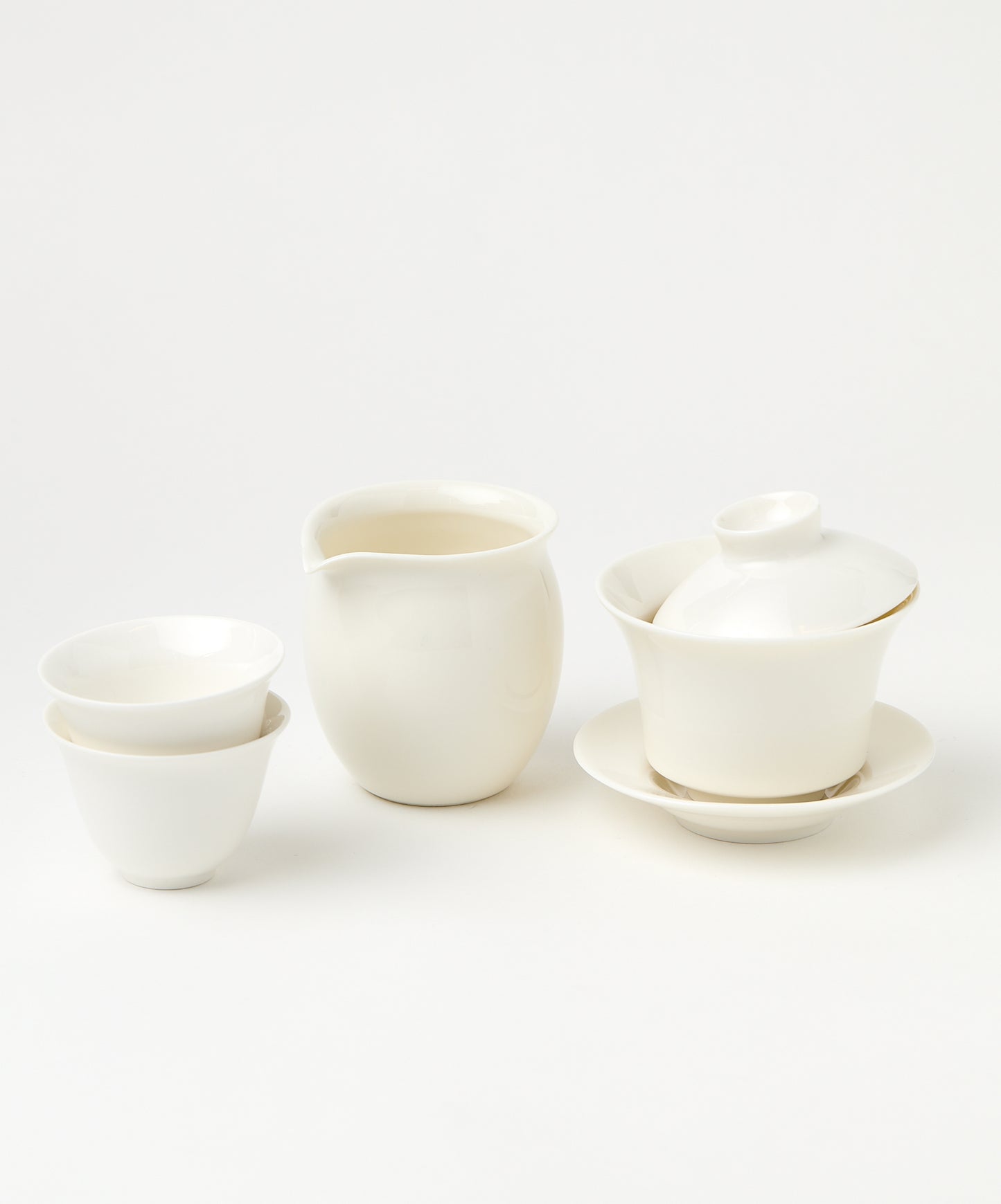 A white porcelain gaiwan with a tilted lid, a pitcher, and two stacked teacups.