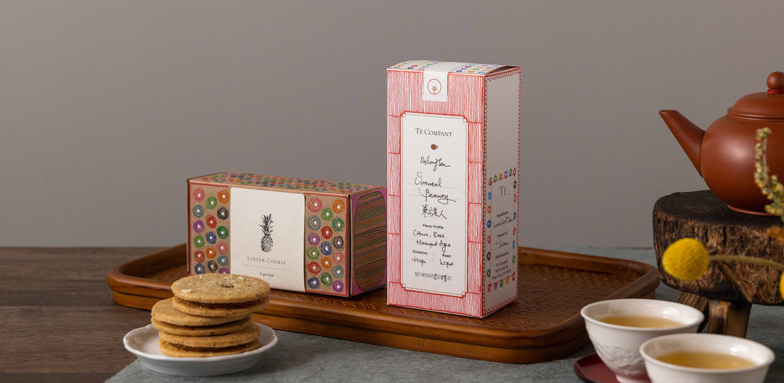 Linzer cookies and tea packaging on wooden tray.