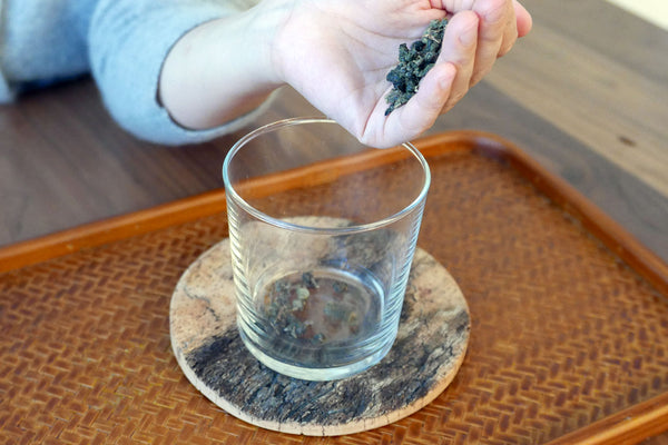 Hand adding loose leaf tea to a glass cup.