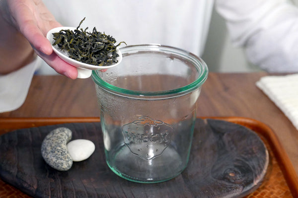 Adding loose leaf tea to a glass brewing jar.