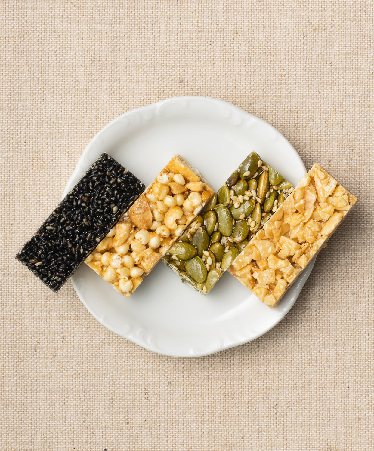 our rectangular seed and nut bars in varying colors and textures, arranged on a white plate against a beige background.
