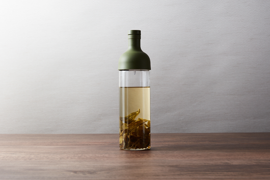 A glass bottle with tea and brewed tea leaves inside.