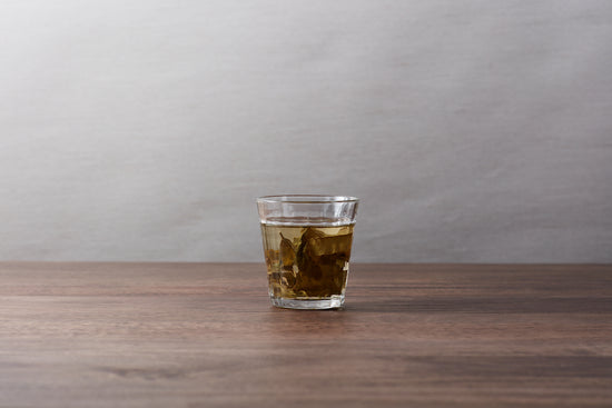 A glass of brewed tea with tea leaves inside.