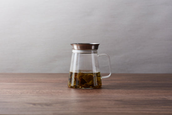 A glass tea server filled with brewed tea and steeped tea leaves.