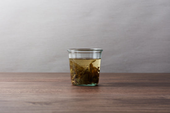 A Weck glass jar with tea and tea leaves inside.