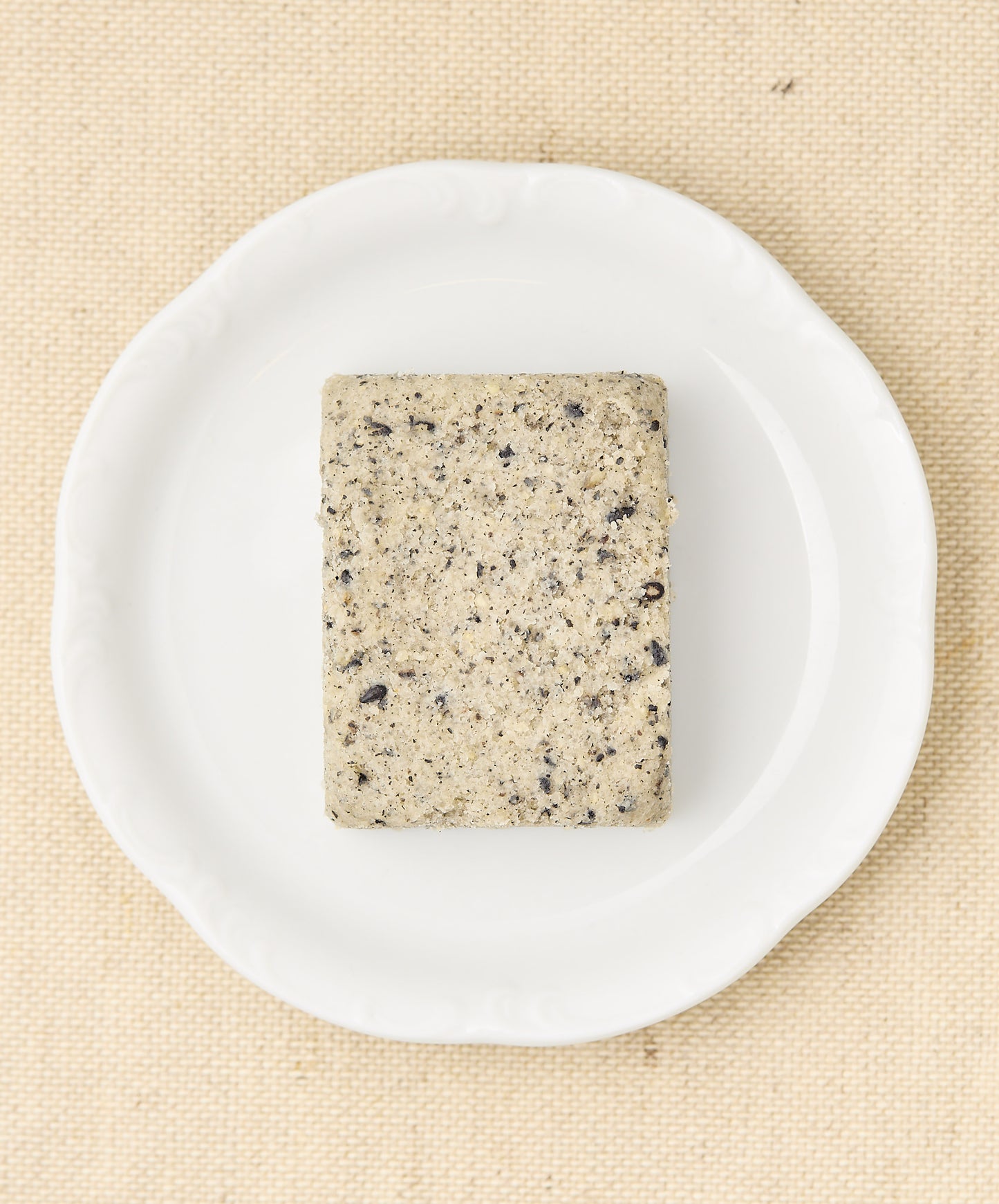 A rectangular block of black sesame cake with a speckled gray surface, sitting on a white plate.