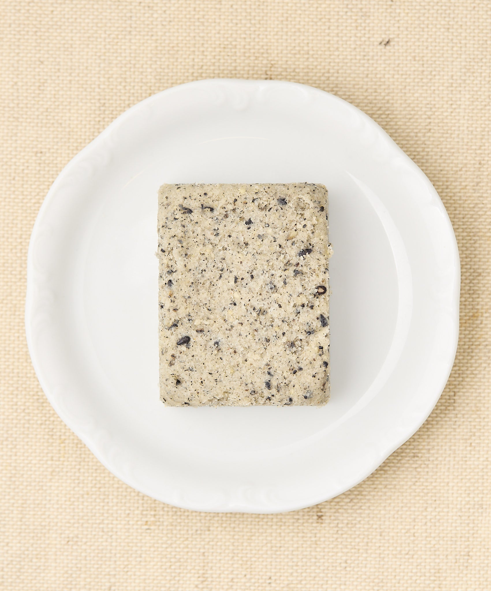 A rectangular block of black sesame cake with a speckled gray surface, sitting on a white plate.