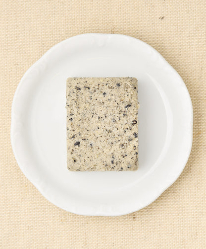 A rectangular block of black sesame cake with a speckled gray surface, sitting on a white plate.