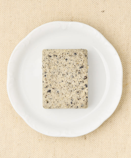 A rectangular block of black sesame cake with a speckled gray surface, sitting on a white plate.