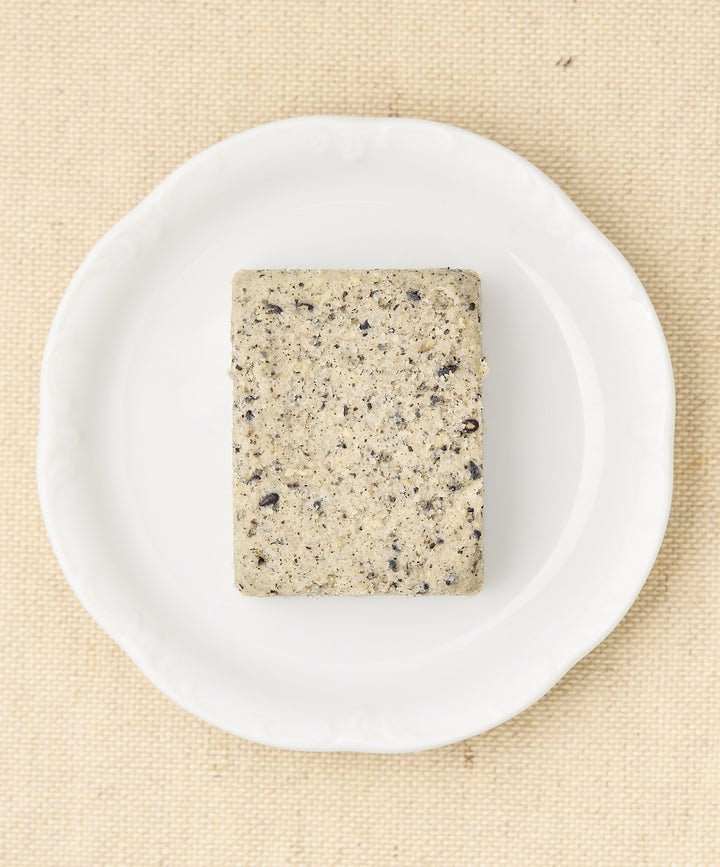 A rectangular block of black sesame cake with a speckled gray surface, sitting on a white plate.