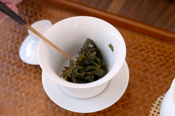 Brewed tea leaves in a white gaiwan on a woven tray.