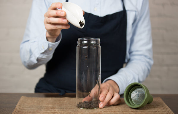 Person pouring loose tea leaves into a glass bottle for cold brewing.
