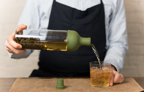 Person pouring cold brew tea from a glass bottle into a cup.