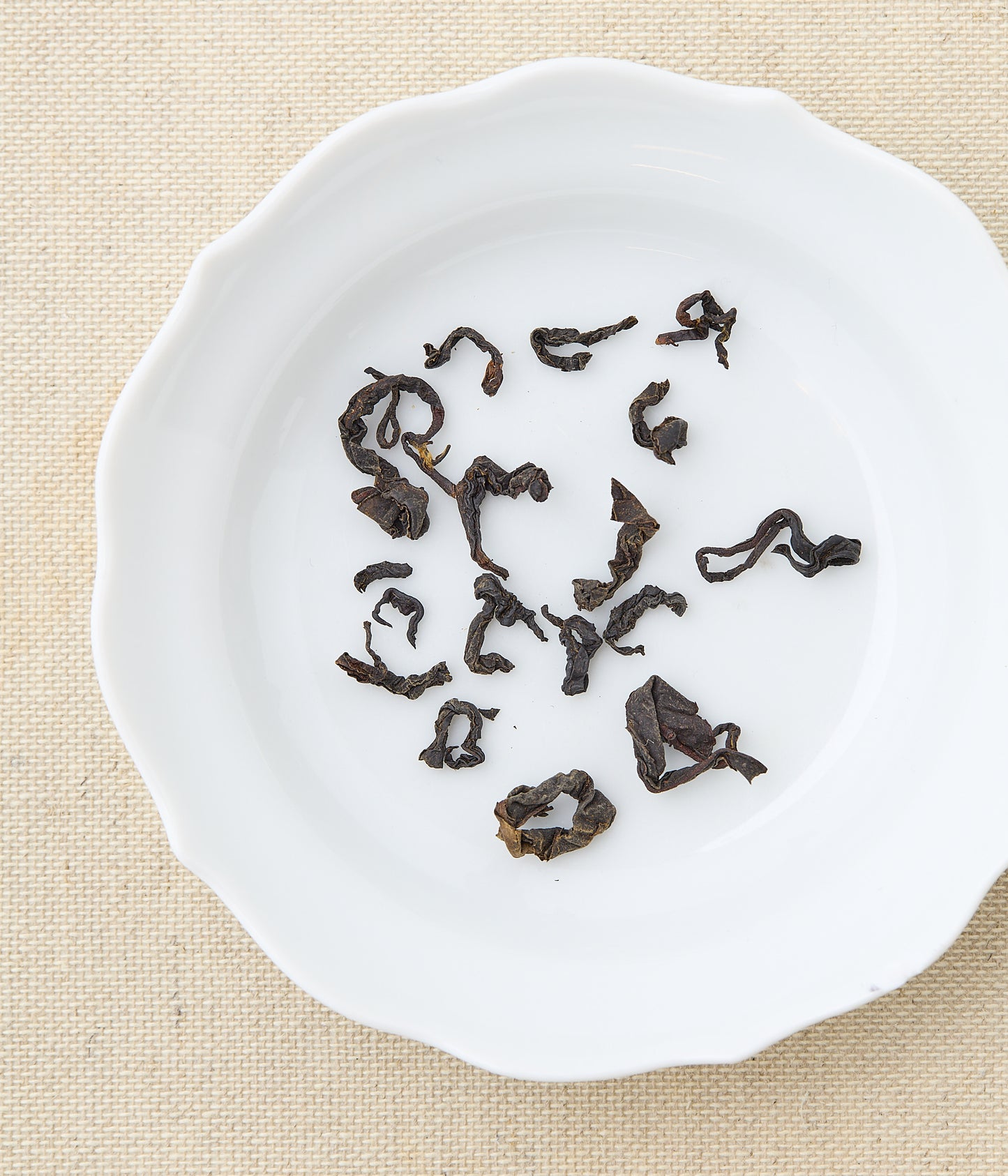 Twisted dry leaves of Honeyed Black tea on a white ceramic plate