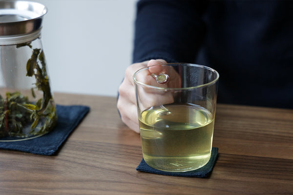 A hand holding a glass cup filled with brewed tea.