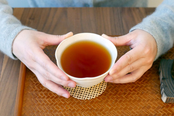 Hands holding a bowl of dark amber-colored tea.