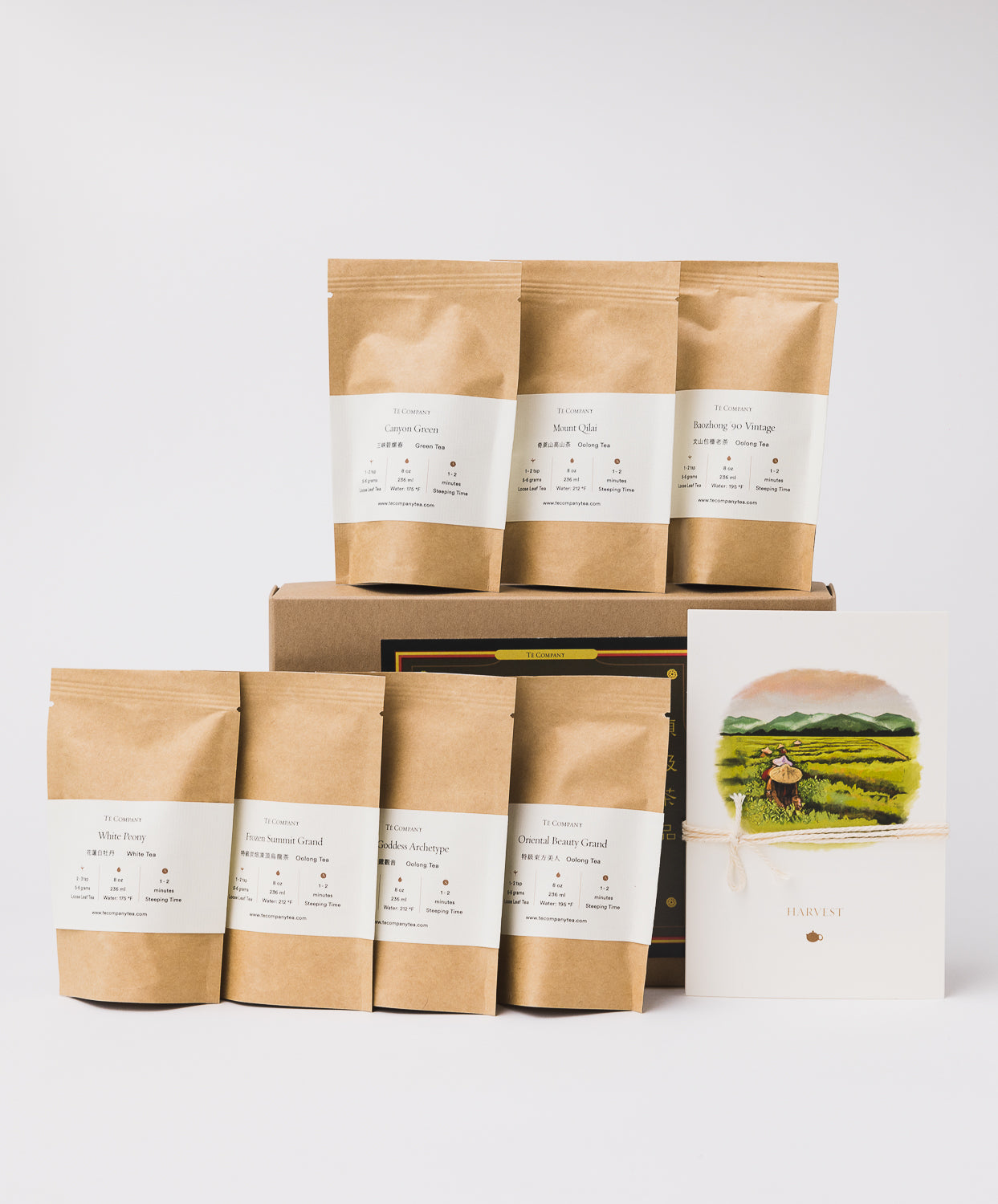 A tea gift set featuring seven brown pouches labeled with different tea varieties, a brown box, and an illustration of a tea harvest scene tied with string.