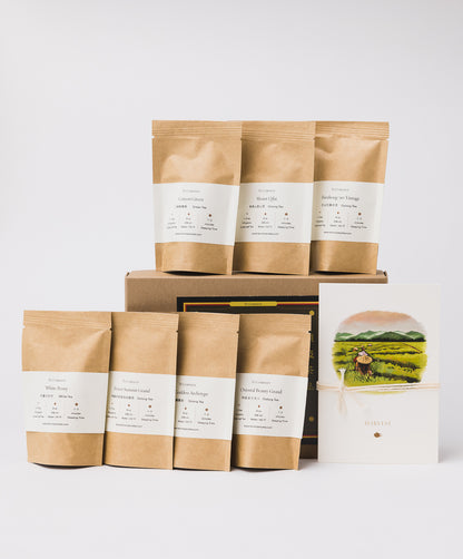 A tea gift set featuring seven brown pouches labeled with different tea varieties, a brown box, and an illustration of a tea harvest scene tied with string.