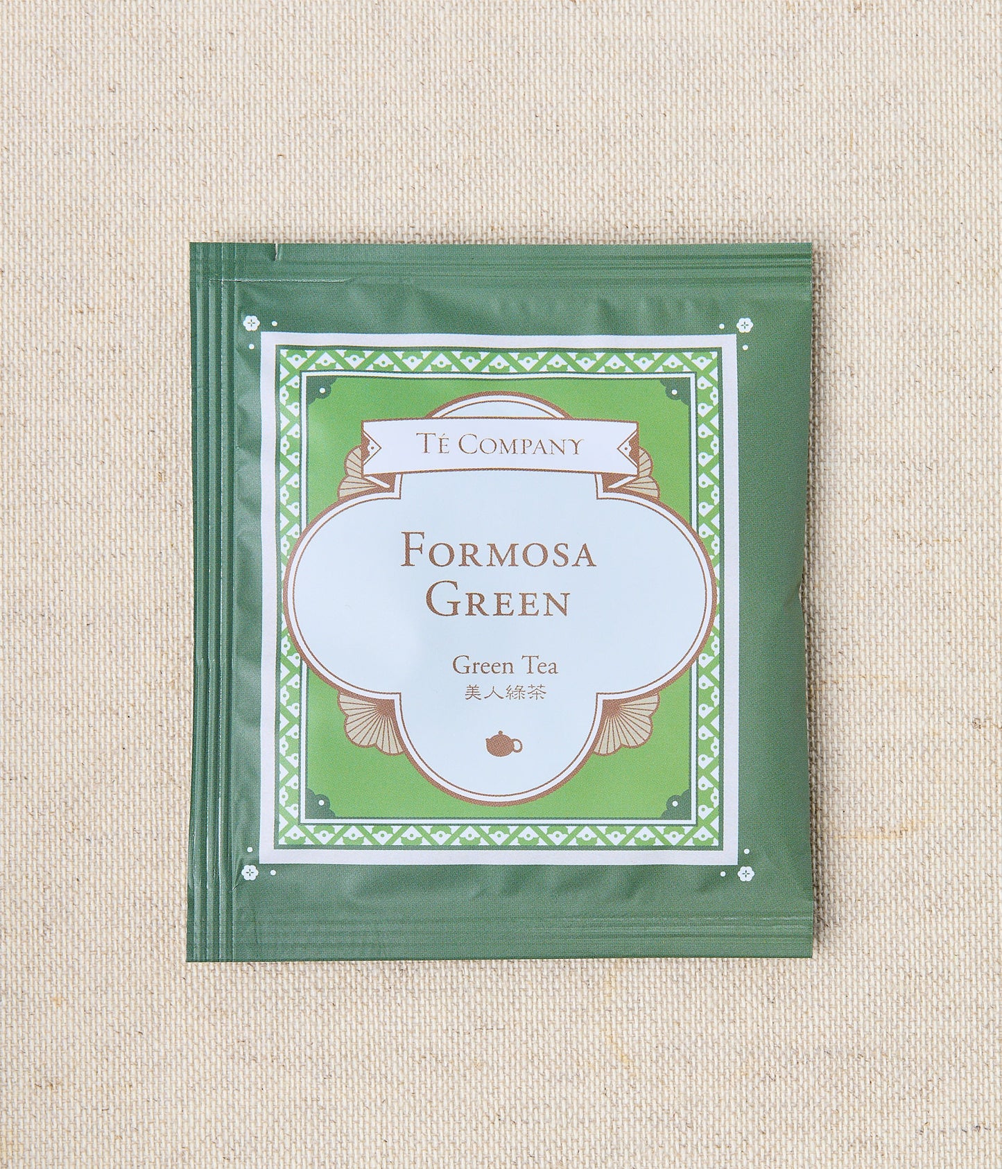 Single packet of Te Company Formosa Green green tea on a beige textured background.