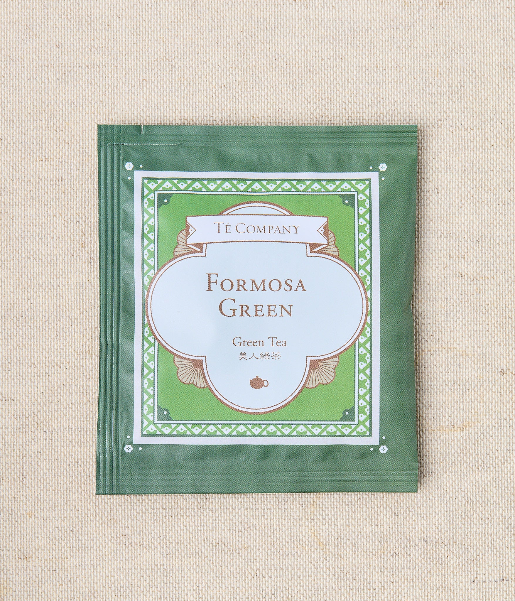 Single packet of Te Company Formosa Green green tea on a beige textured background.