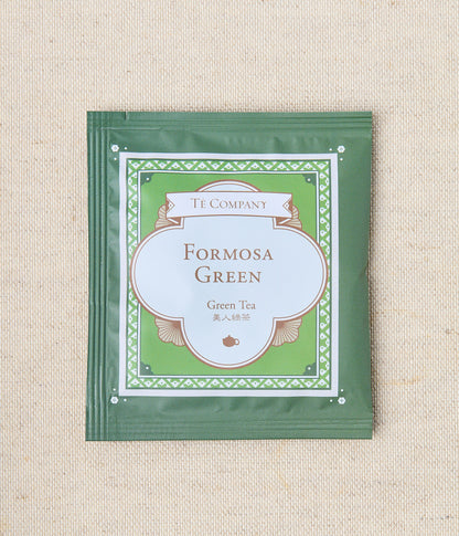 Single packet of Te Company Formosa Green green tea on a beige textured background.