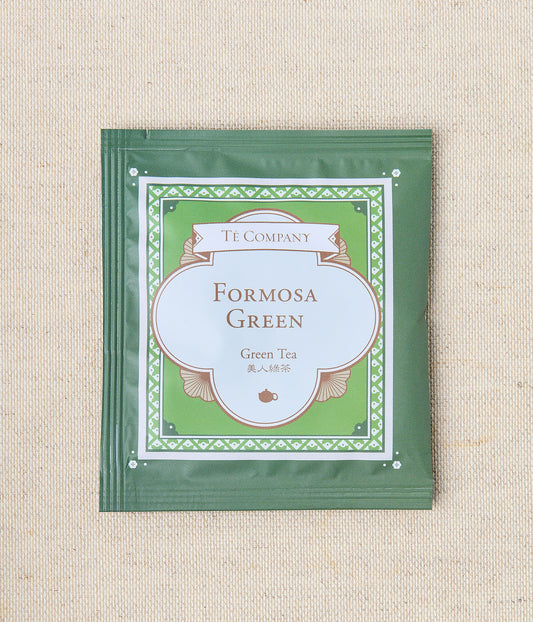 Single packet of Te Company Formosa Green green tea on a beige textured background.
