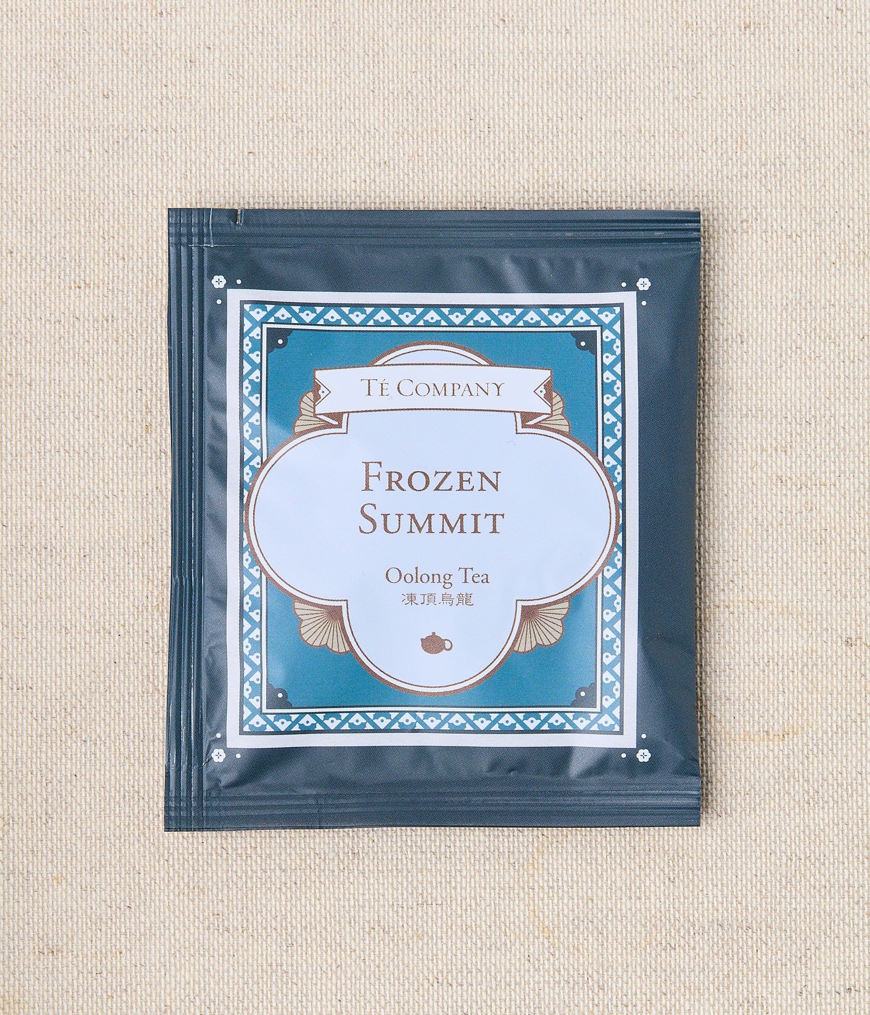 Single packet of Te Company Frozen Summit oolong tea on a beige textured background.