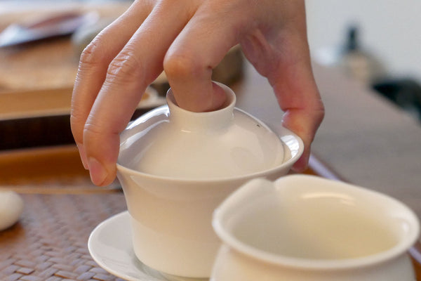 Hand holding the lid of a gaiwan while preparing tea.