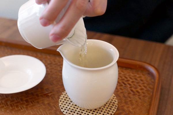 Person pouring tea from a gaiwan into a white pitcher.