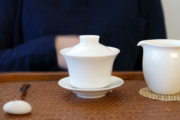 Gaiwan steeping tea with the lid on a wooden tray.