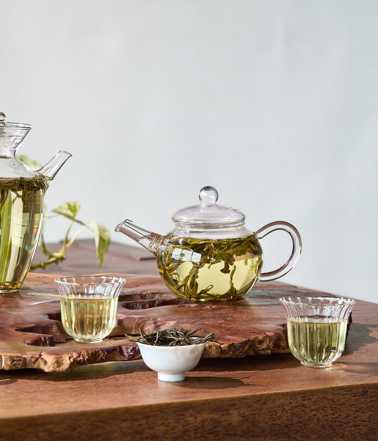 Tea-making setup with glass teapot, cups, and tea leaves on a wooden board.