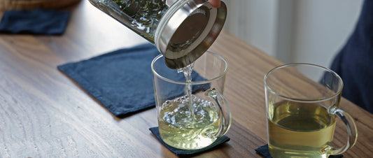 Pouring tea from a glass tea brewing pitcher into a clear cup.