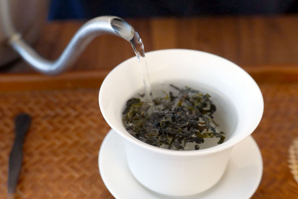 Hot water being poured over tea leaves in a gaiwan.