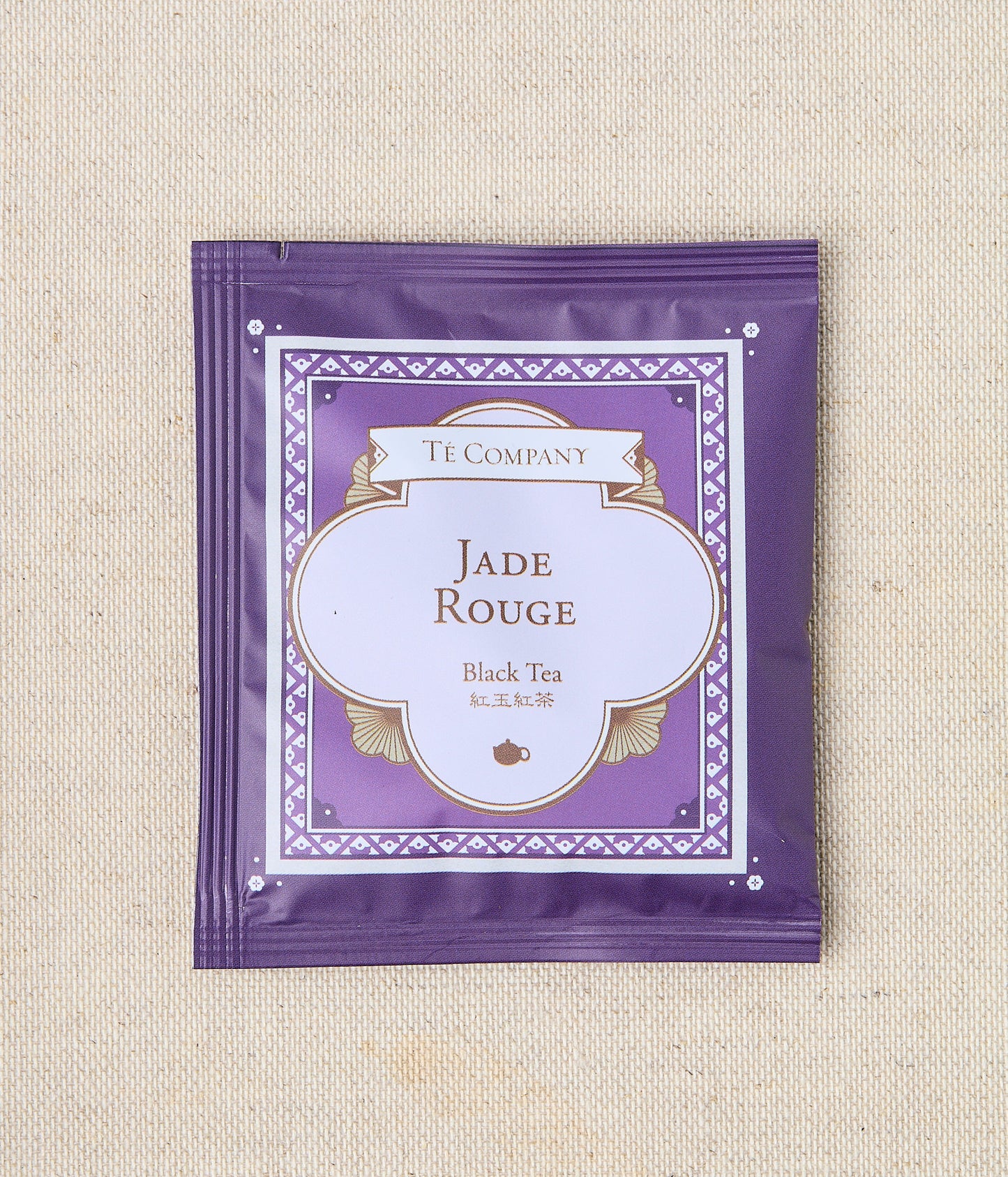 Single packet of Te Company Jade Rouge black tea on a beige textured background.