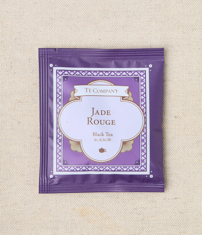 Single packet of Te Company Jade Rouge black tea on a beige textured background.