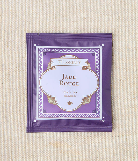 Single packet of Te Company Jade Rouge black tea on a beige textured background.