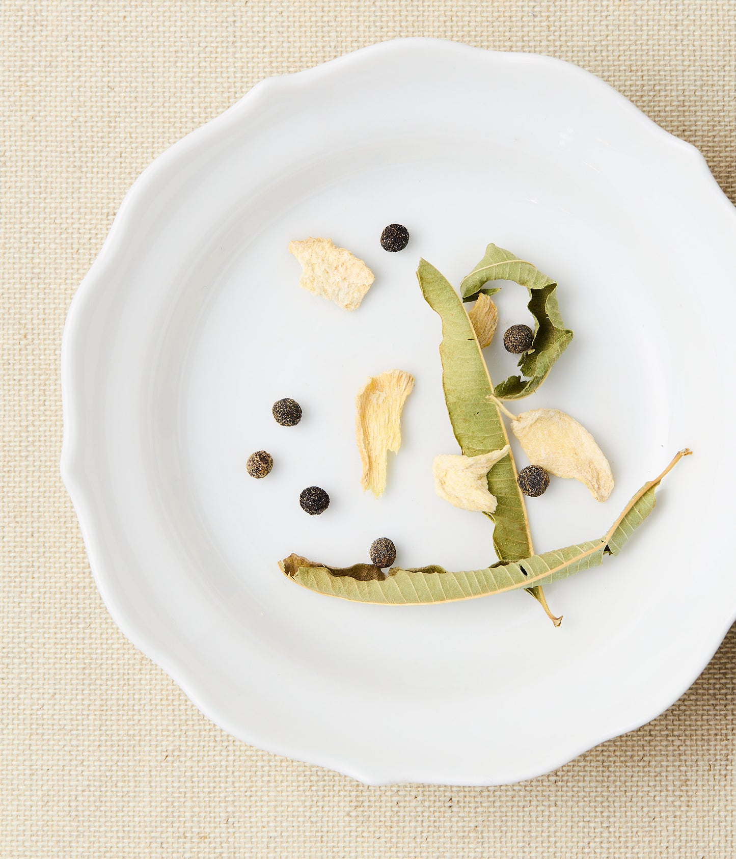 Dried leaves, ginger, and maqaw peppercorns on a white plate.