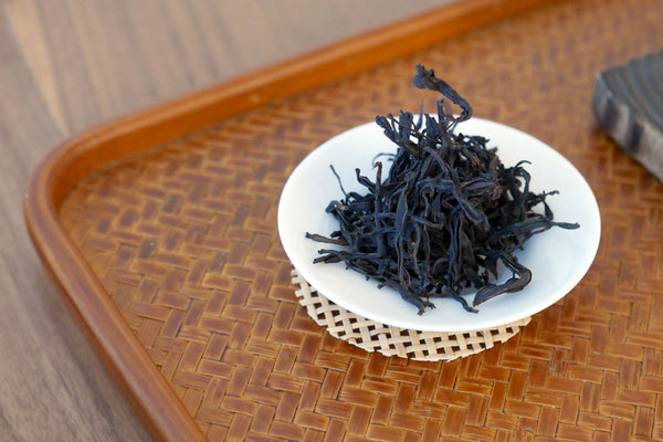 Loose leaf tea on a small white dish on a woven tray.