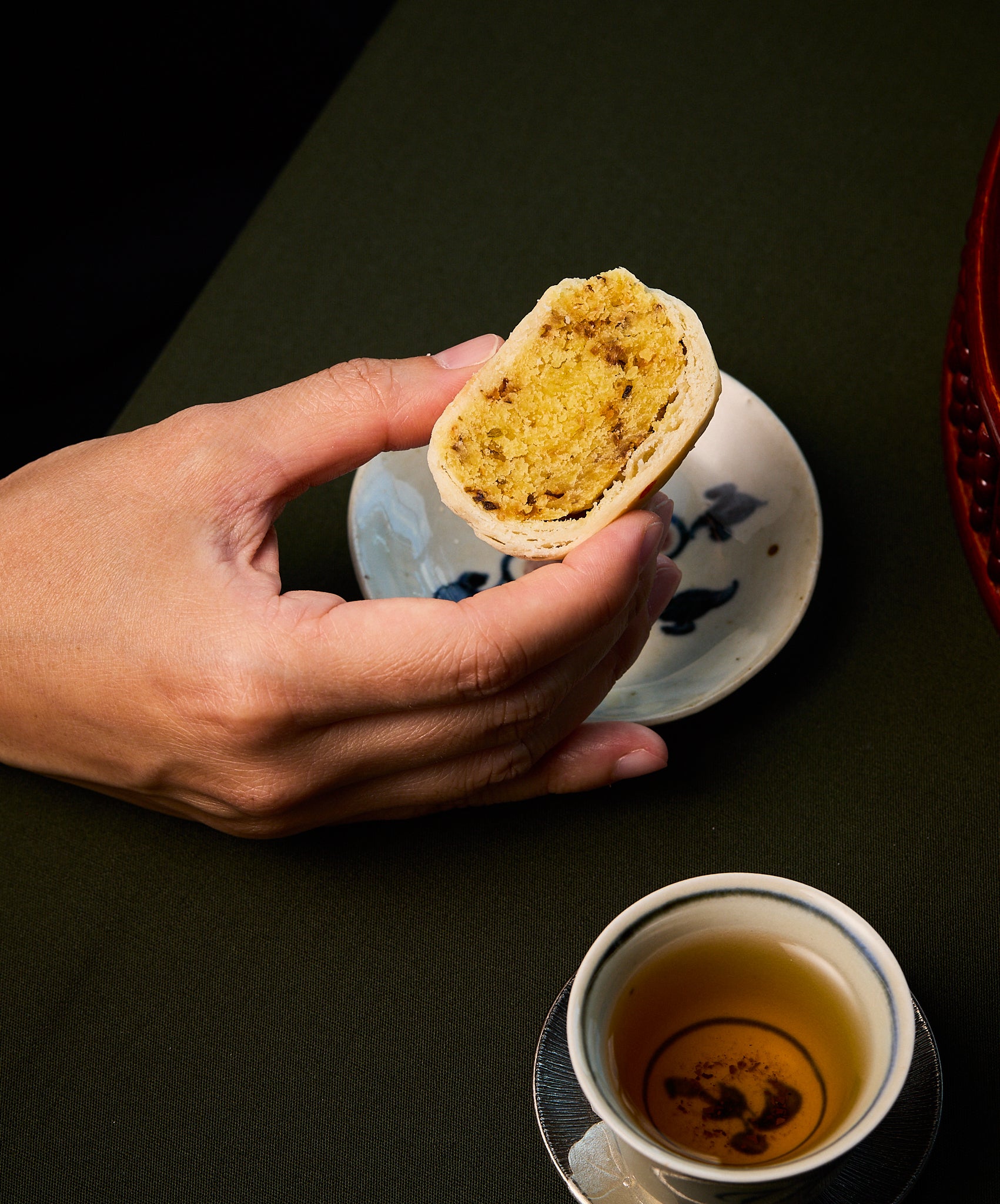 Person holding a half-eaten pastry with a cup of tea on a dark surface