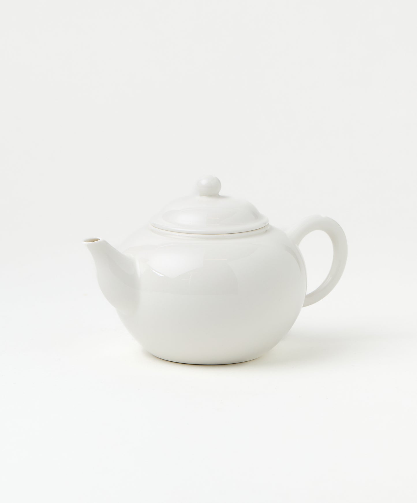 Side view of a white porcelain teapot with a smooth, rounded body, a curved spout, and a loop handle.
