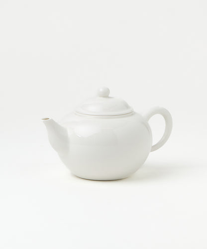 Side view of a white porcelain teapot with a smooth, rounded body, a curved spout, and a loop handle.