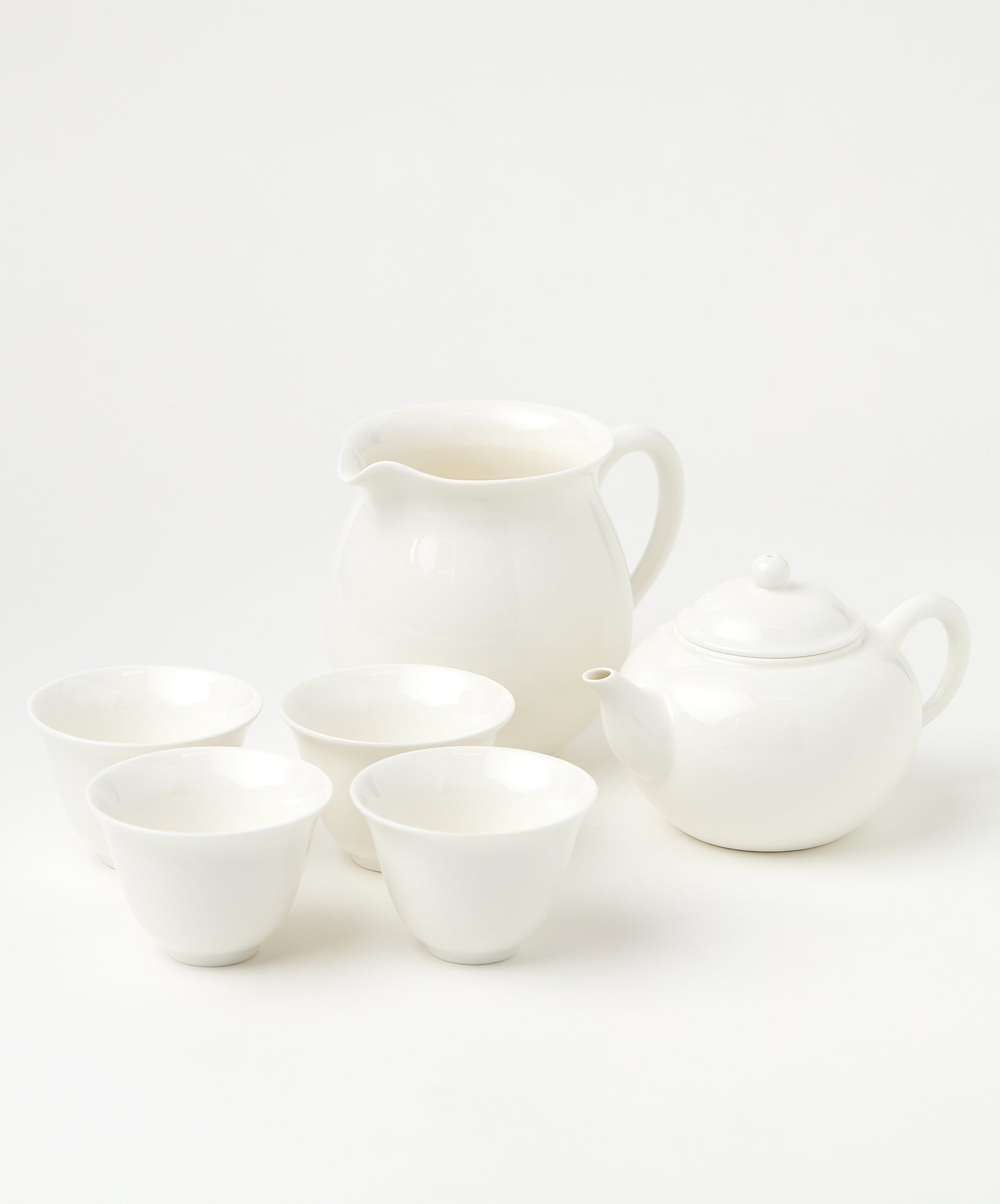 A porcelain brewing set with a white teapot, four matching cups, and a pitcher arranged neatly.