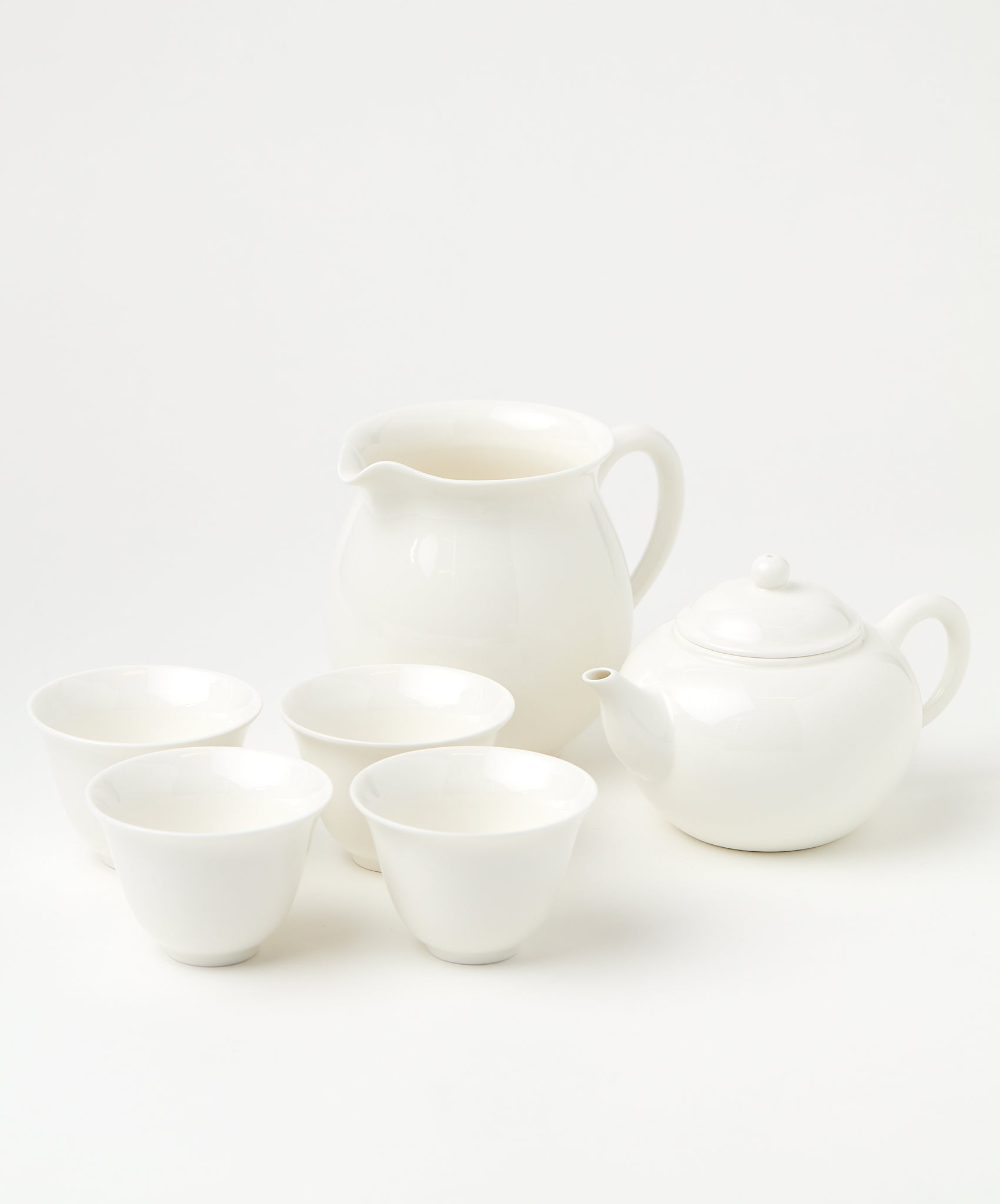 A porcelain brewing set with a white teapot, four matching cups, and a pitcher arranged neatly.