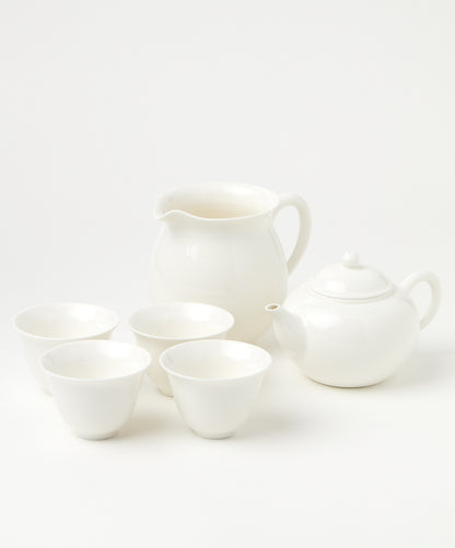 A porcelain brewing set with a white teapot, four matching cups, and a pitcher arranged neatly.