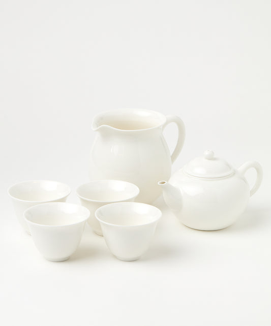 A porcelain brewing set with a white teapot, four matching cups, and a pitcher arranged neatly.