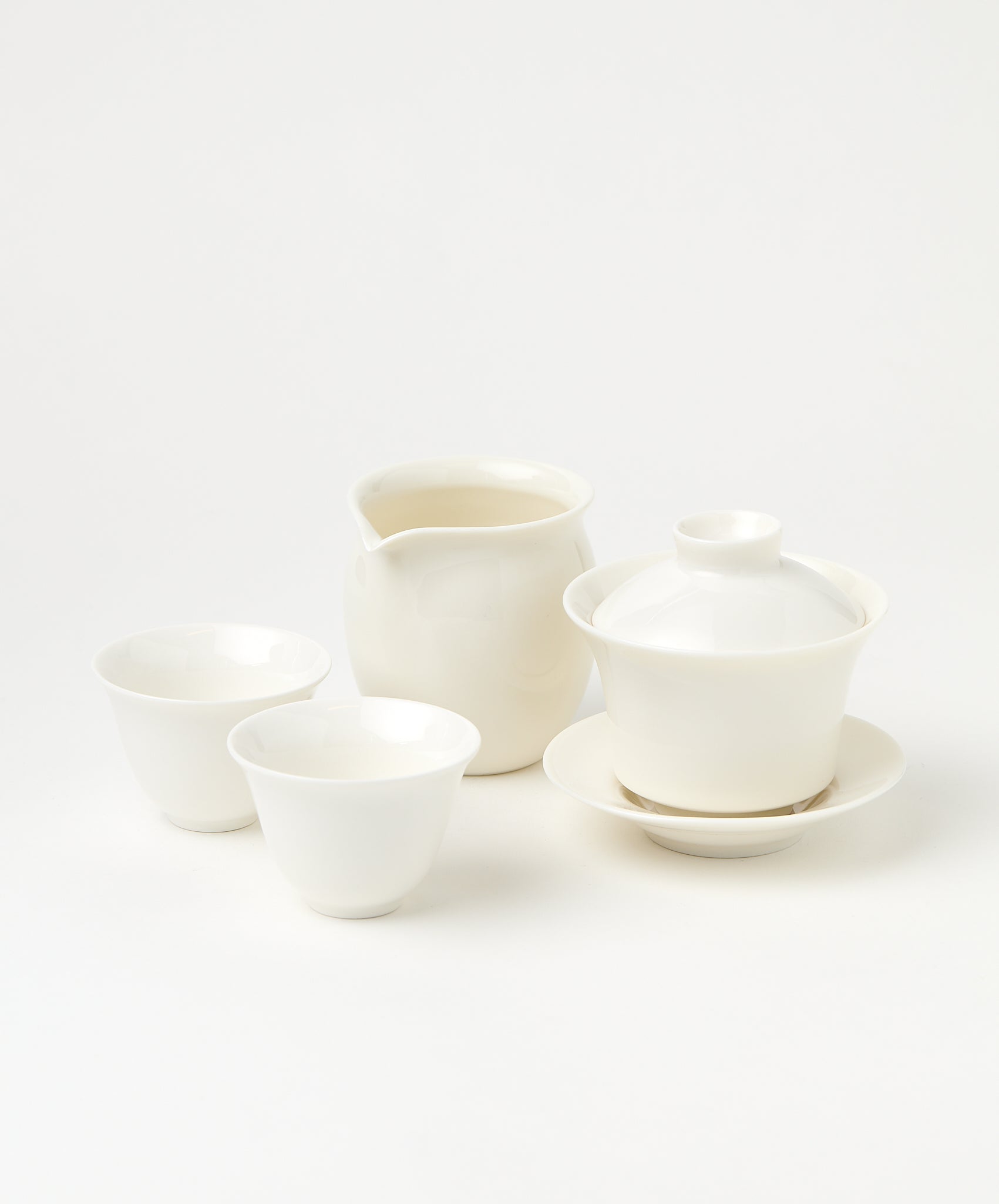 A white porcelain gaiwan with a lid and saucer, a pitcher, and two teacups.