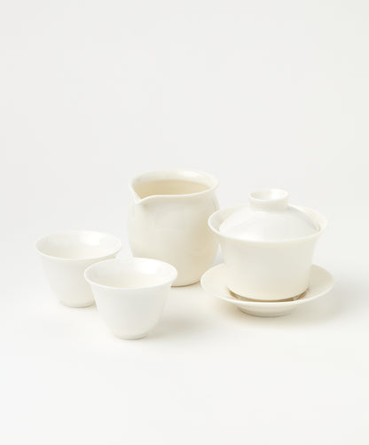 A white porcelain gaiwan with a lid and saucer, a pitcher, and two teacups.