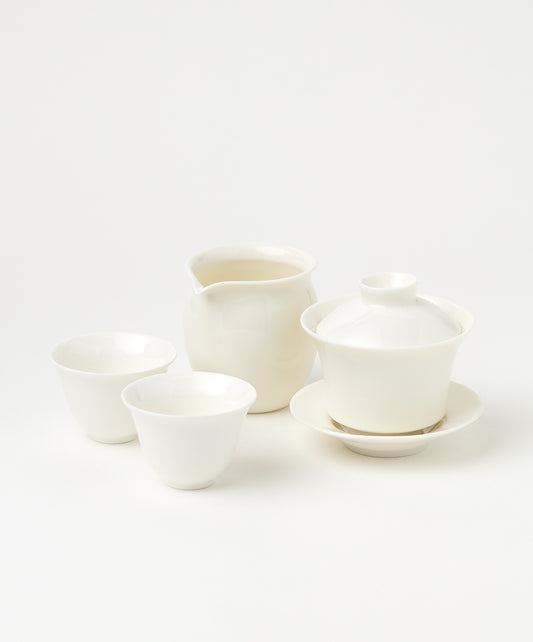 A white porcelain gaiwan with a lid and saucer, a pitcher, and two teacups.