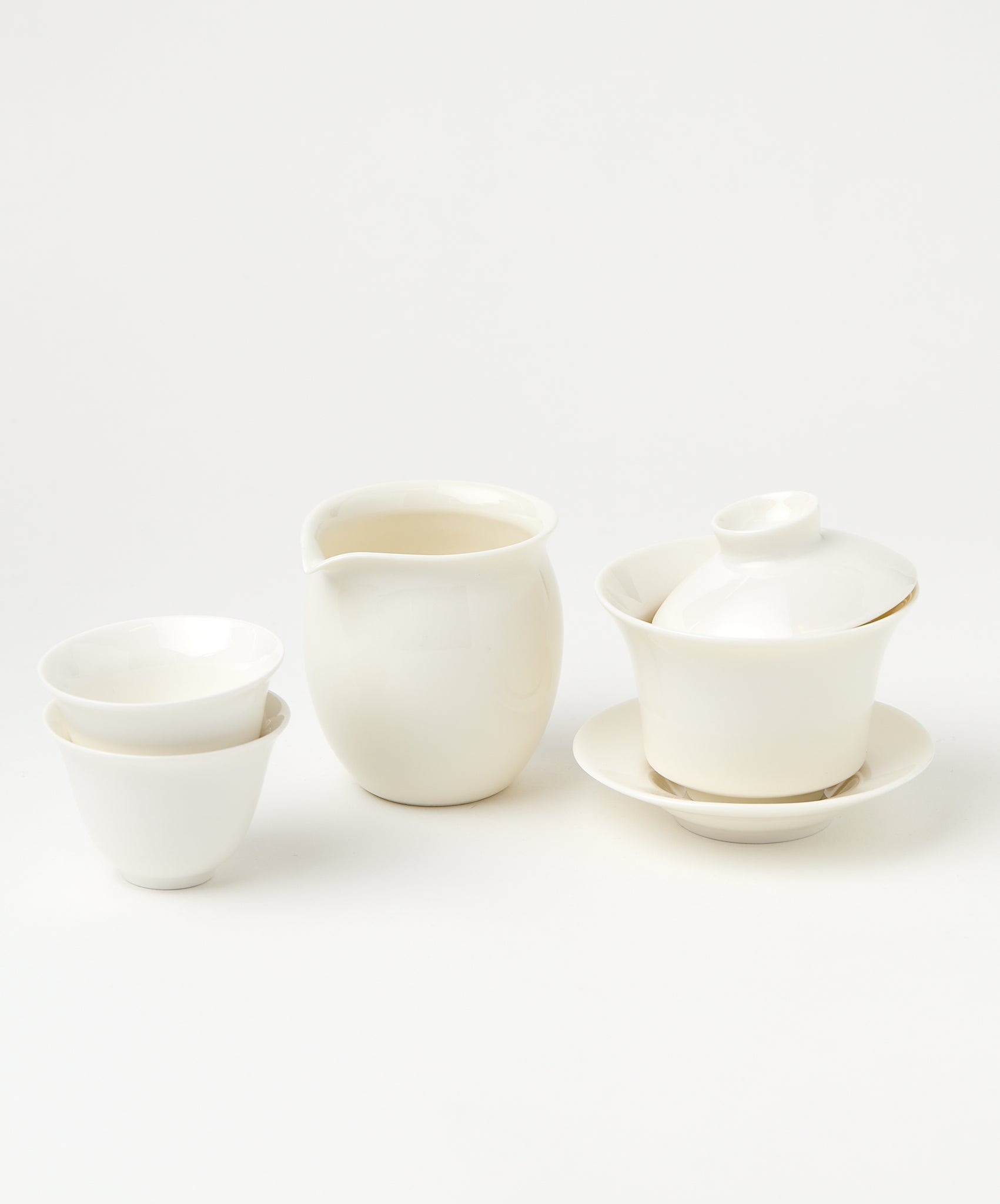 A white porcelain gaiwan with a tilted lid, a pitcher, and two stacked teacups.